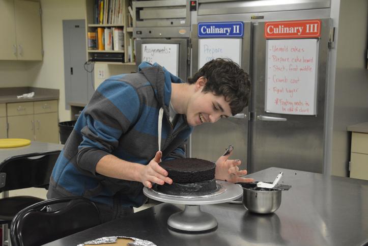 Senior Jeff Guttin centers his top section after frosting the bottom layer. The Culinary 3 classes make cakes for the Purple Party to be used as prizes in the Cake Walk event.