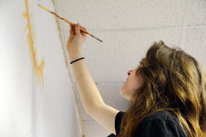 Junior Cameryn Berridge paints over her sketch on the mural which depicts a meteor crashing into Earth by starting out with the bright orange and yellow flames. After making the decision about joining the project after some debate, she now spends her study halls working on the piece. 