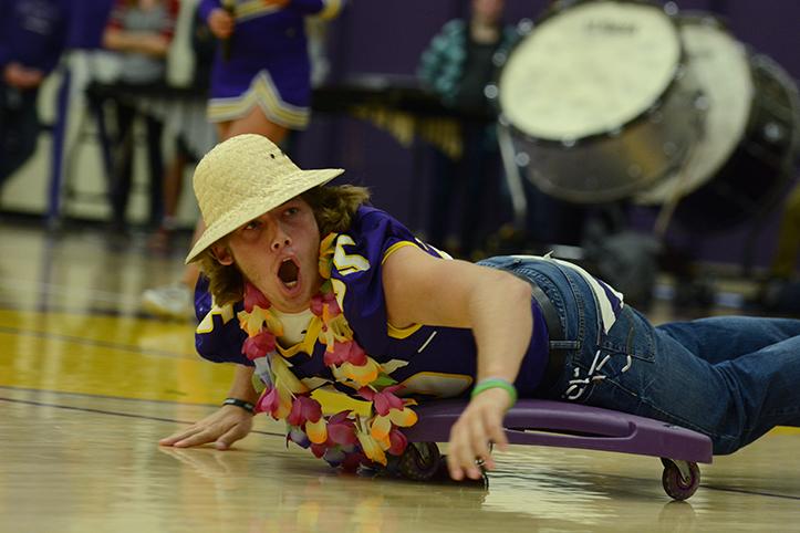 Senior Nolan Monthei yells at the crowd while rolling across the floor on a scooter to compete in the obstacle course. The pep assembly was right after third period Oct. 2 with homecoming festivities such as a teacher lip sync battle and obstacle course.