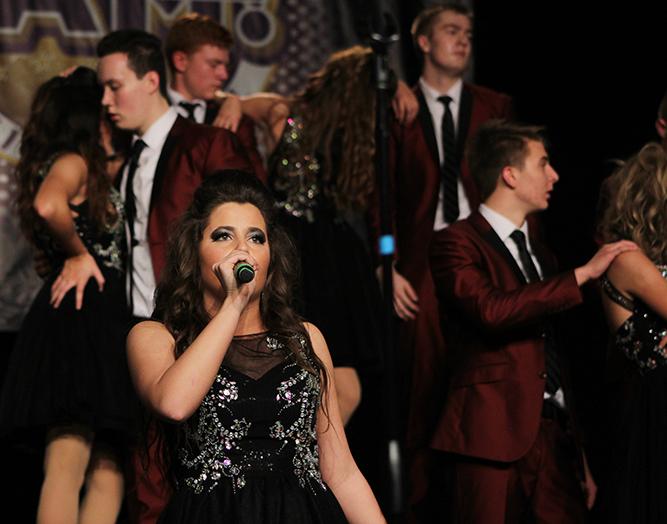 As members of the choir pose behind her, Amanda McGowan 18, performs her solo during Feeling Good Melody. McGowan was able to complete her solo before the fire alarms went off.