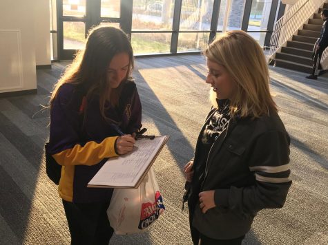 Josie Barsness '18 watches as Anika Schmitt '18 signs the petition she created for the handprint wall.