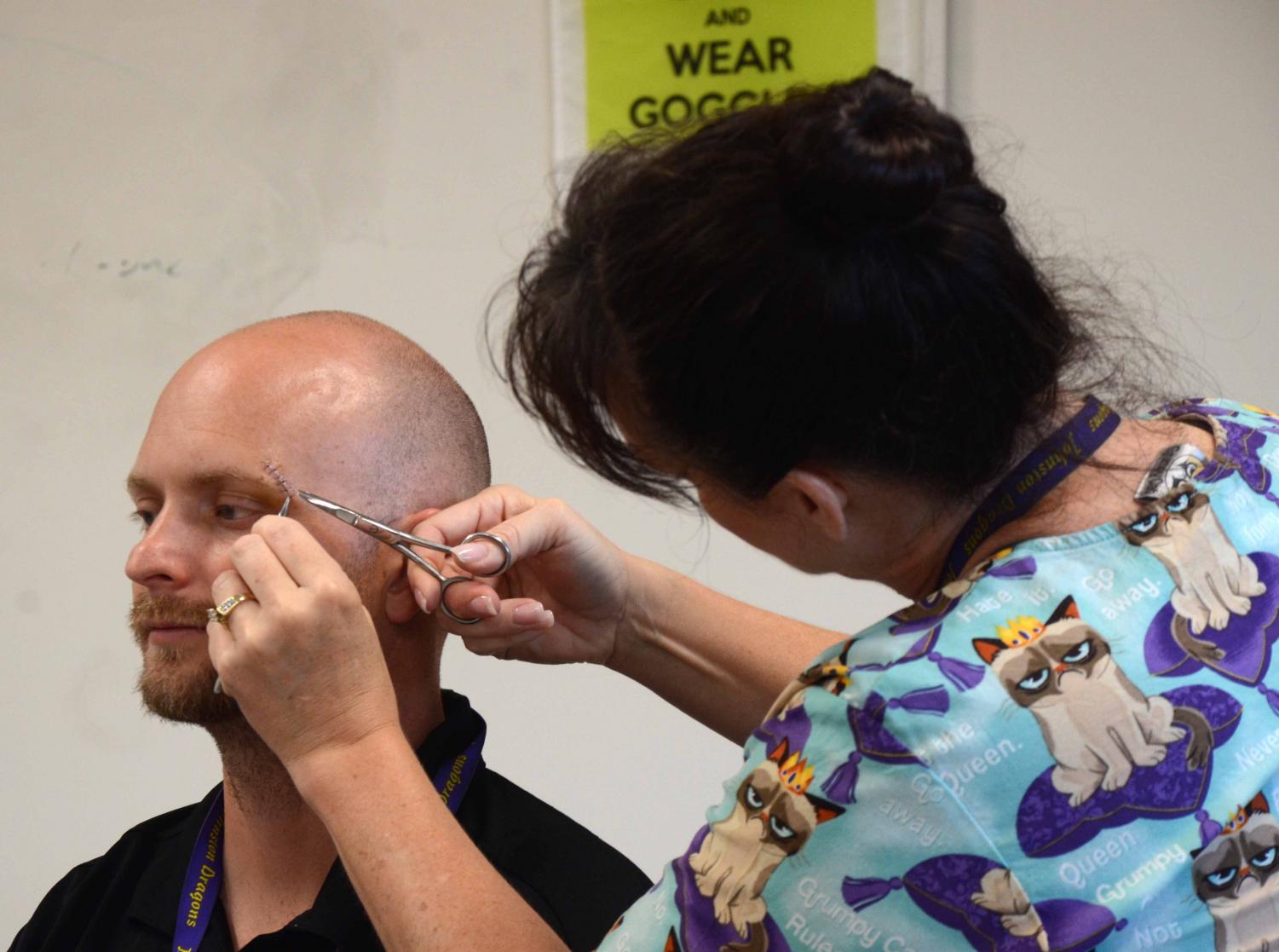 Anatomy teacher Jennifer Lehman removes Chemistry teacher Dave Oldham's stitches. Lehman started her class on a test before leaving the classroom to entertain Oldham's AP Chemistry students.