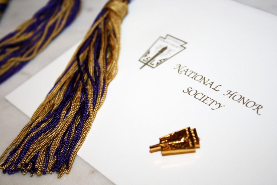 A National Honor Society (NHS) certificate lays next to a NHS pin and the cord NHS members receive at graduation.