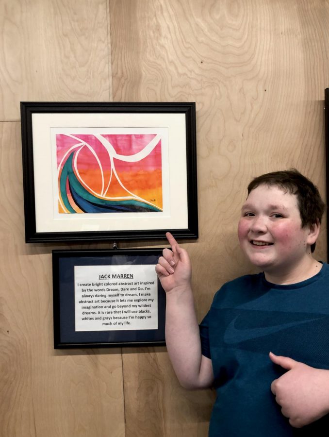 Jack Marren 22 poses for a photo next to his piece that won the t-shirt design contest at the art show at Mainframe Studios on Sep. 6. Underneath the artwork is a statement that he wrote about why he loves this type of art.