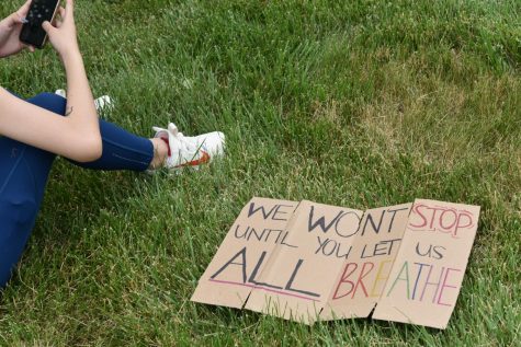 A student sets down their sign crafted from a cereal box as they wait for instruction. Community members staged a march at the middle school June 26 to address inequality and racism in the district.