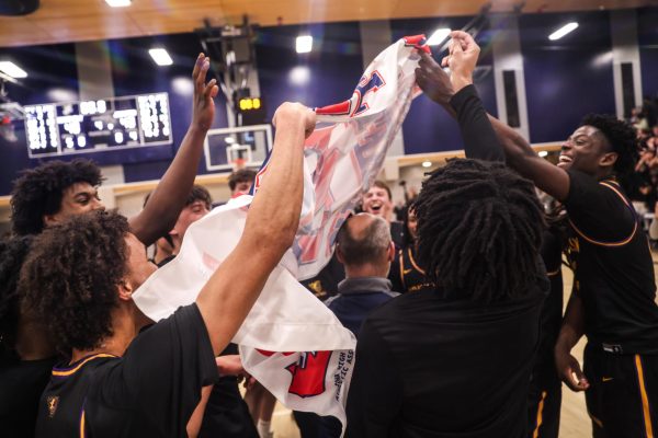 Johnston players gather and celebrate with the state qualifier banner following their 43–40 win over Roosevelt in the substate final on March 3 at Roosevelt High School. The victory sends the Dragons back to the state tournament for the first time since 2024.